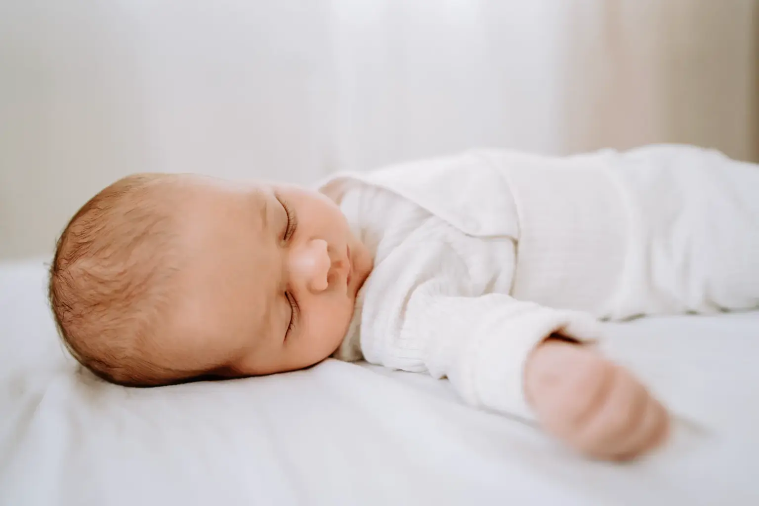 Süßes, cleanes Babyfoto auf einer weißen Decke in einem cleanen Setting im Fotostudio in Weilheim
