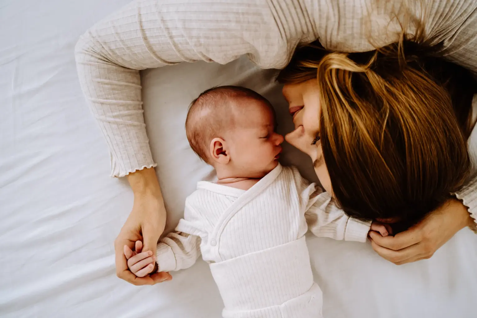 Mama kuschelt mit ihrem Baby und liegt auf einem Bett mit weißem Laken