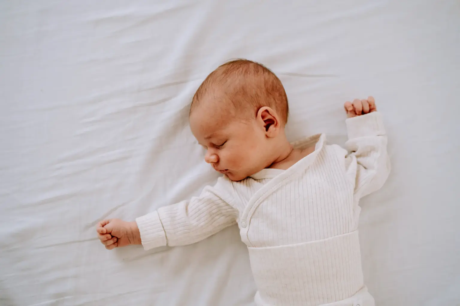 Baby liegt schlafend auf einem weißen Laken