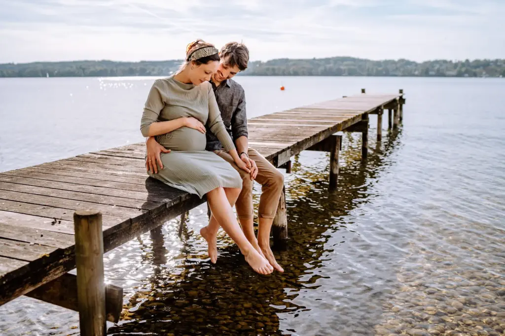 Paar sitzt auf dem Steg, Füße nah am Wasser, Babybauchfoto
