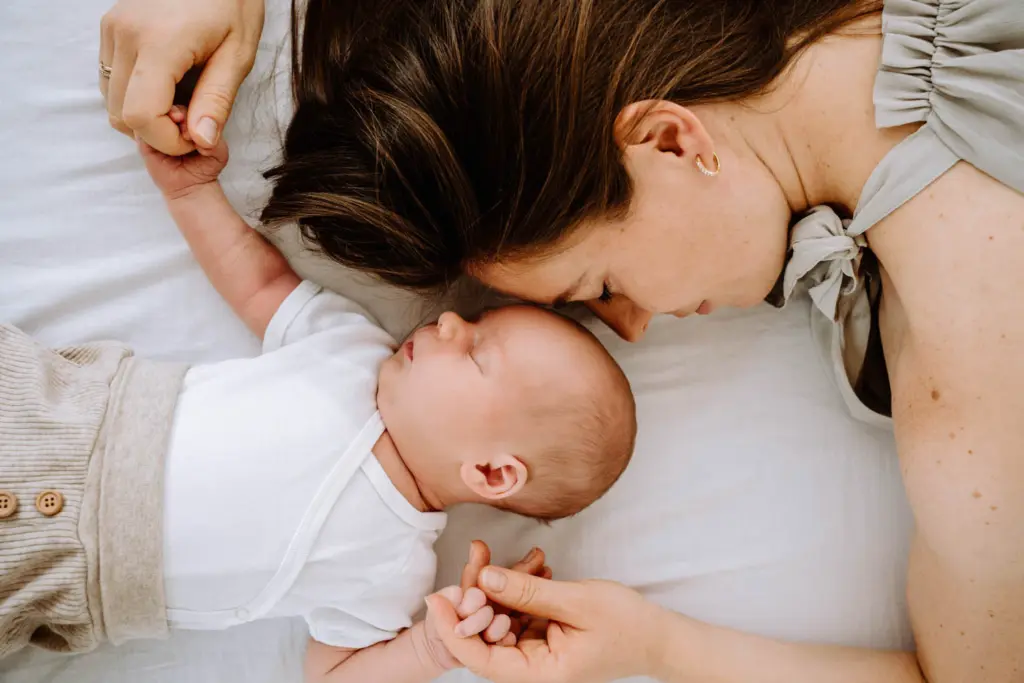 Mama liegt neben ihrem schlafenden Baby und hält die Hände fest